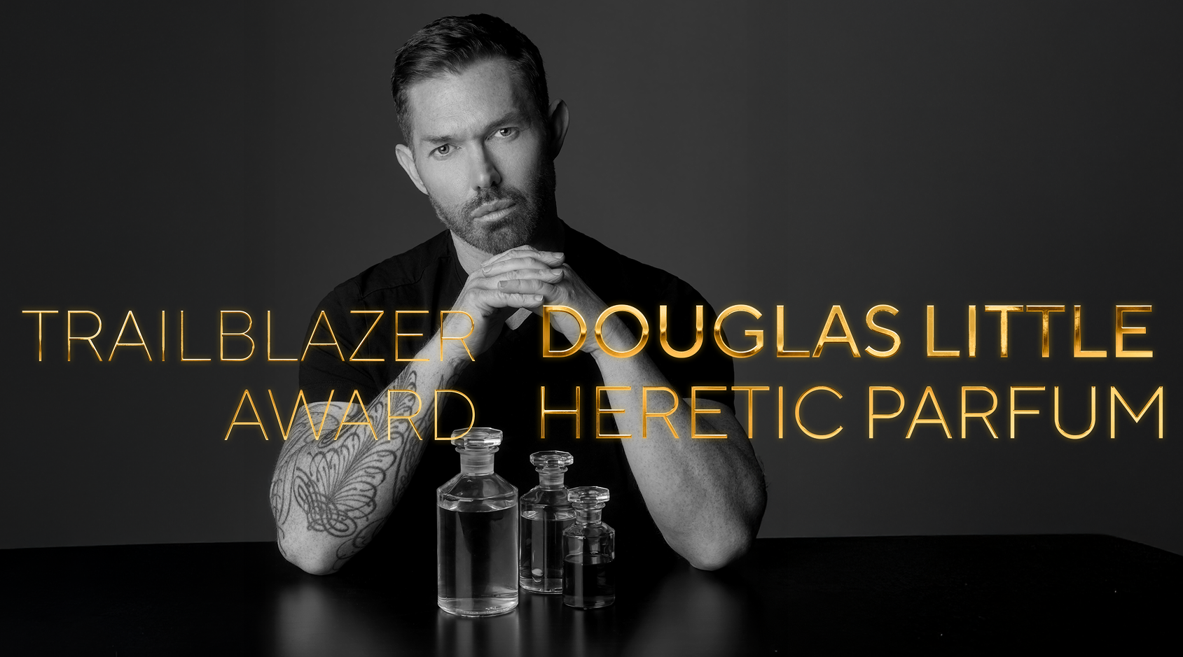 Portrait of Douglas Little seated with fragrance bottles, with Trailblazer Award and Heretic Parfum text overlaid.