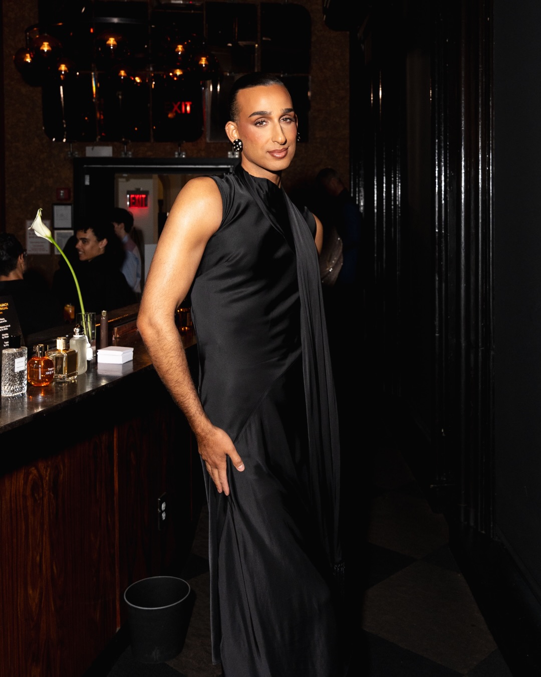 Cyrus Veyssi, host of the Scentbird Digital Fragrance Awards, standing beside a fragrance display in a black sleeveless outfit.